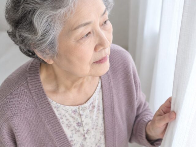 커튼 가장자리를 잡고 옆을 바라보는 80대 어머니